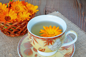 Marigold herbal tea and flower on wooden table.